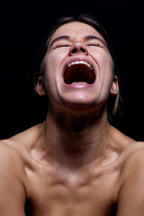 Screaming woman on a black background. Young woman's face with mouth open while screaming isolate from black. She is frustrated and in emotional pain. She is stresed and mad.