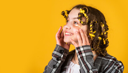 Happy child with eye patches. Little girl curlers around her hair. Create beautiful hairstyle. Gorgeous hairstyle. Hairdresser salon. Girl with curlers and hair clips in her hair on yellow background