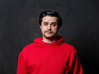 White sad guy in red sweatshirt on dark background