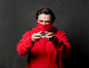 guy in red sweatshirt and face mask hold game controller on dark background