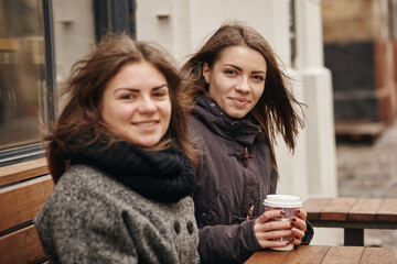 Outdoors fashion portrait of two young beautiful women friends drinking coffee.