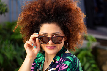 Chica de cabello churco posa con sus lentes de sol en una tarde de verano 