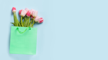 Tulips flowers in green paper bag on blue. Top view with copy space. Spring flowers delivery.
