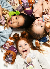 Children kids playing in kindergarten girls lying on a floor with little doll toys happy screaming laughing. Top view