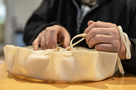 Very close up of man's hands creating a hand tambourine with a piece of leather, pulling and tying the end, during a native drum workshop.