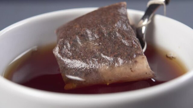 A teaspoon with a teabag is dipped in hot water and brews the tea in a white cup. Macro shot