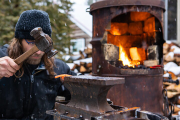 Close up shot of a young man, very concentrated in hammering a red, sizzling hot rod of iron out of...