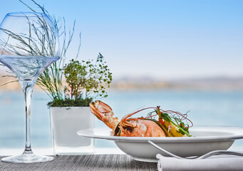 Close up detail of plate with wine glass shrimp overlooking the sea