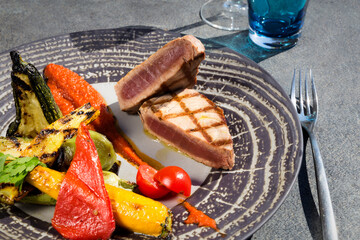 Close up and detail of grilled tuna slice with grilled vegetables and gray concrete table