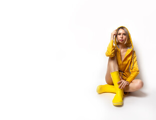 Horizontal banner with young woman in illuminating yellow slicker and rubber boots. Fashion blonde girl sitting on white background. Spring and autumn clothes