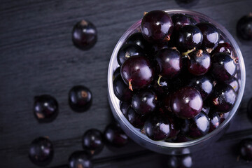 Black currant and green leaves on a dark wooden background. Background with currant berries and green leaves. Currant Macro.
