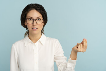 Female telling you to pay debts and taxes. Businesswoman in glasses wearing white blouse doing money rich gesture with hand, asking for salary payment, cash or allowance. Studio blue background.