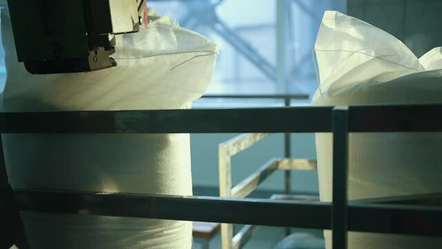 Full white bags lie on the conveyor belt. Sugar packing in plastic bag conveyor line. Briquettes food industry plant. Sugar beet factory