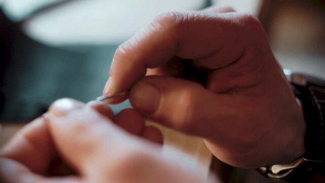 Close-up of male hands threading a needle and tying a knot in workshop