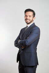 A smiling young Latino businessman standing in a dark gray suit and tie on a white background