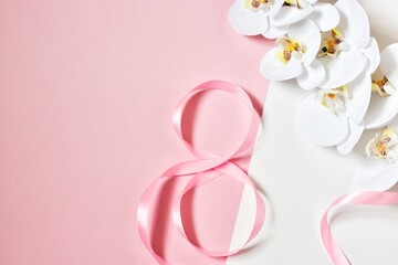 The pink ribbon lies in the form of 8 with an orchid flower on a white-pink background. Concept woman's Day.