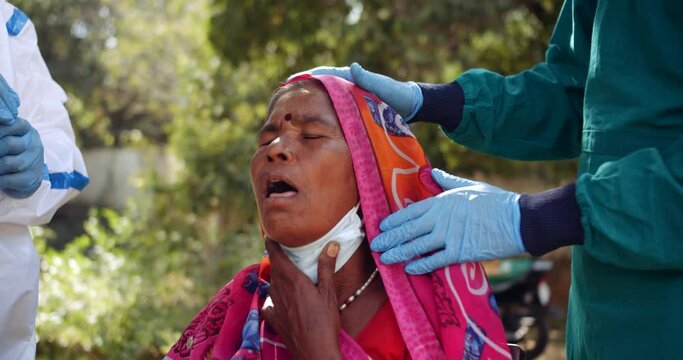 Close-up slow-motion of medical staff with medical gloves takes samples from inside throat of an old woman in red colorful saree for virus examination collection with protective workwear gear in India