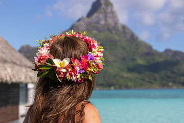 Naklejka premium Woman wearing colorful flower crown looks at Mt. Otemanu while on vacation at beautiful tropical island Bora Bora in French Polynesia