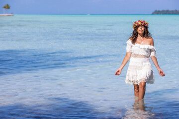 Fototapeta na wymiar Woman wearing colorful flower crown stands in shallow clear turquoise ocean water while on vacation at beautiful tropical island Bora Bora in French Polynesia