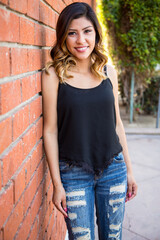 Hispanic young woman standing against a red brick wall wearing ripped jeans