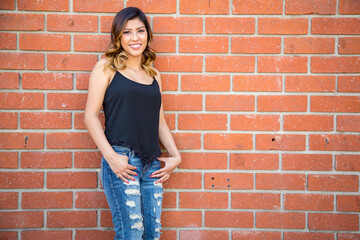 Hispanic young woman standing against a red brick wall wearing ripped jeans