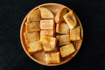 Thai Condensed Milk Toast served on wooden plate on black table.