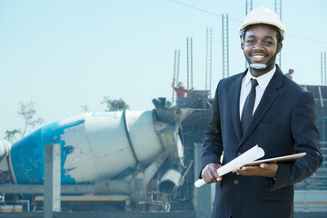 Portrait of African  site contractor engineer with hard hat holding blue print paper and tablet with building in background