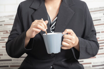 Close-up businesswoman hand holding a mug of coffee and stirring.