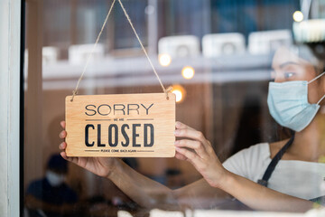 Young asian owner retail,coffee shop woman turning sign board to closed with wearing face mask,protection to pandemic of coronavirus.Close store,restaurant or pub due to lockdown, quarantine of covid. - Powered by Adobe