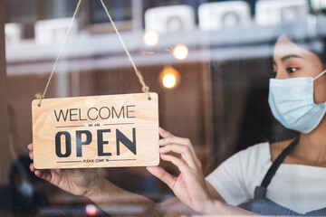 Owner retail,coffee shop woman turning sign board to open with wearing face mask ,protection to...