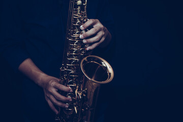Close up of a young musician man hands hold and playing saxophone on black background with copy...
