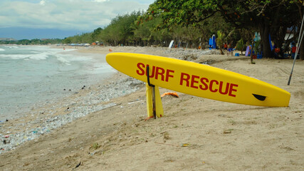 Yellow surfboard on beach with red text surf rescue emergency on a beach