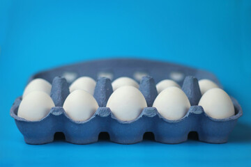 White chicken eggs in a color paper tray on a blue surface, selective focus