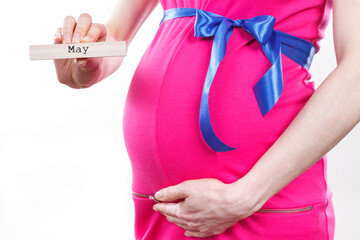 Woman in pregnant wearing pink dress with blue ribbon and showing word may. Expecting for newborn and expansion of family