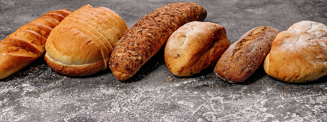 Fototapeta na wymiar Food baking banner. Various types of fresh homemade bread on a gray concrete background. Horizontal shot