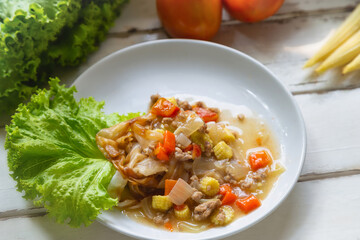 Flate noodle with minced pork sauce on a white plate on a white wooden table with baby corn and tomato and .Lettuce background.