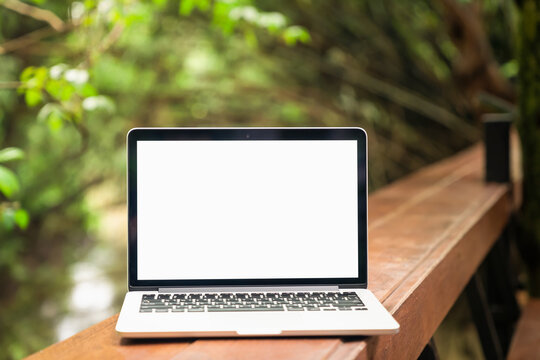 Laptop screen is blank are placed on a wooden table and trees with nature that are beautiful on a light rainy day.