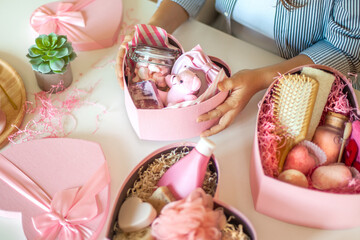 Woman preparing pink colored heart shaped gift boxes with organic natural cosmetics of body care