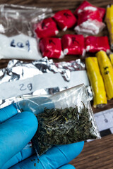 Fototapeta na wymiar evidence of smuggling traffic: Packaging of a narcotic substance in the hand of a forensic expert against the background of other arrested materials, cocaine, heroin, spice