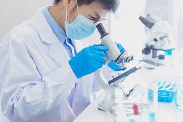 Male Scientist look into Microscope research in science laboratory. Asian scientist looking equipment laboratory chemistry labs. Covid-19 coronavirus biochemistry research experiment vaccine concept