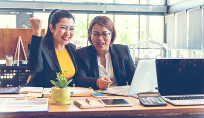 Happy success business woman partner working together in company office corporate executive teamwork. Meeting Executive Asian business woman using laptop office desk with fist arm raised win happiness