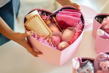 Woman hands holding pink colored heart shaped gift boxes of bath and body products for bridesmaids.