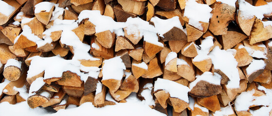 The stacked firewood for the stove is covered with snow.
