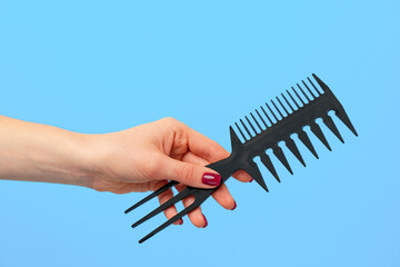 Female hand holding hair comb against blue background