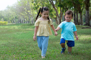 Sister and brother holding hands and walking on the green lawn in the summer