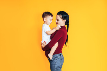 Pregnant young woman holding a small baby in front of a yellow background. Caring for the health of a pregnant woman. Artificial insemination
