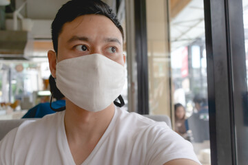 Fototapeta na wymiar Asian man wears white mask for Covid virus protection in public cafe.