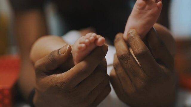 Black father playing with baby feet. Close up slow motion. High quality 4k footage