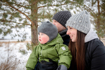 A family with a small child laughs in the park in winter. Happy family.