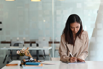 A young female creative designer concentrate working on digital tablet while sitting in modern office.